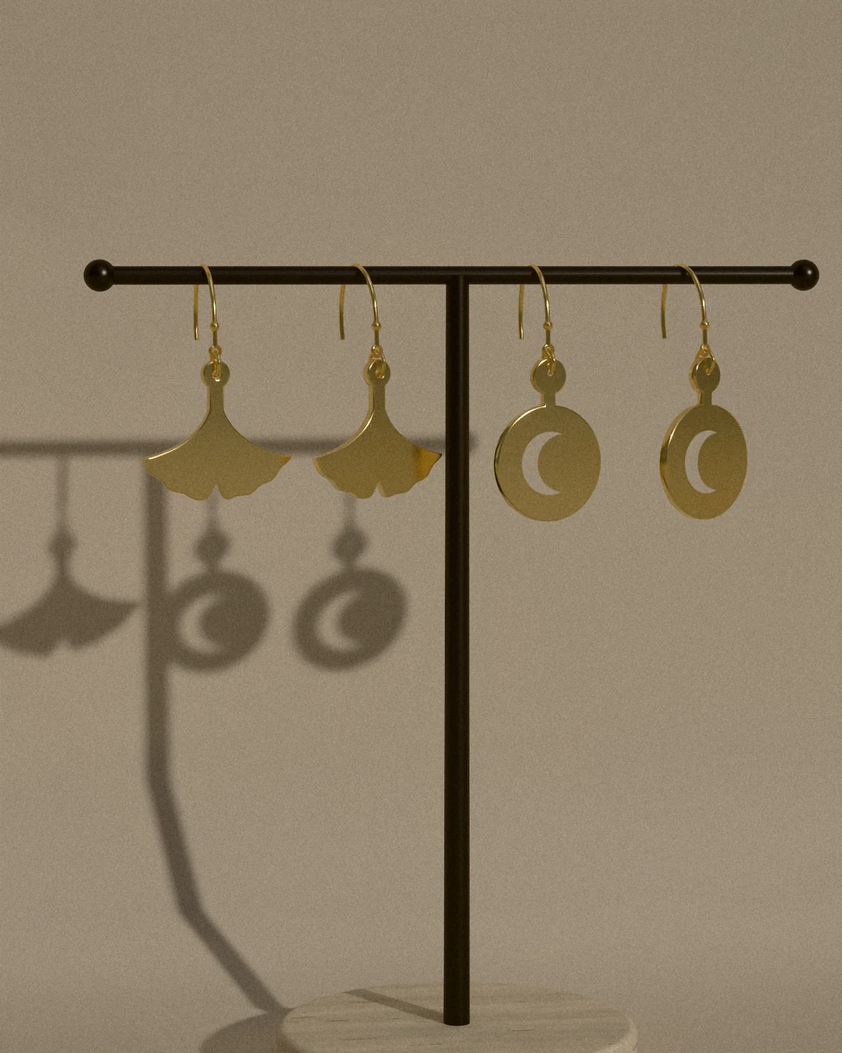 Ginkgo and crescent earrings hanging from a bronze stand, their shadows on the wall