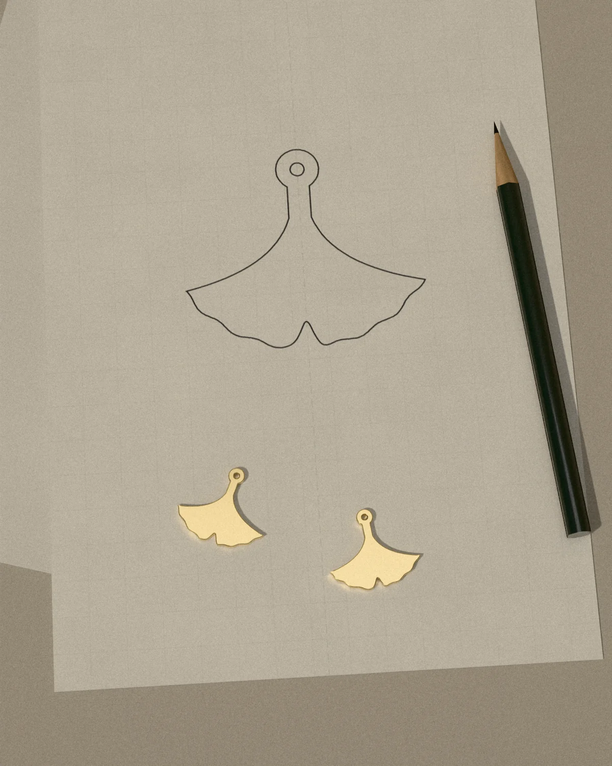 A ginkgo drawn in pencil on vellum, the brass earrings cut from it laid beside, and a pencil